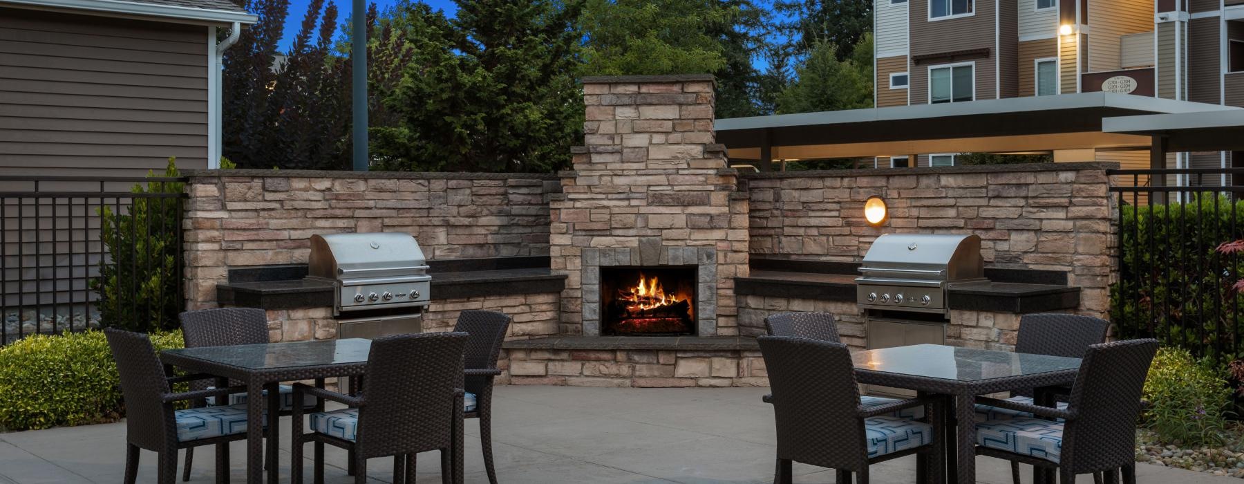 a patio with a fire pit and chairs and a brick wall