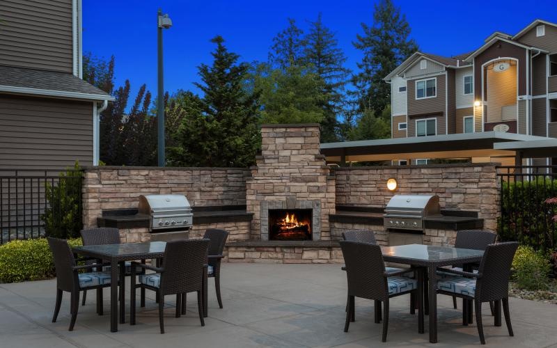 a patio with a fire pit and chairs and a brick wall